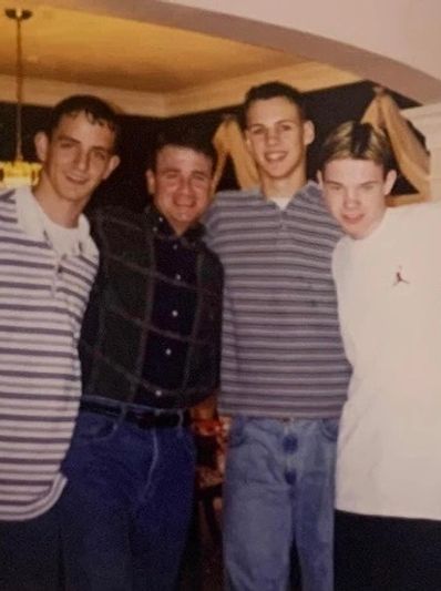 A group of six young men posing indoors, dressed in 90s casual fashion.