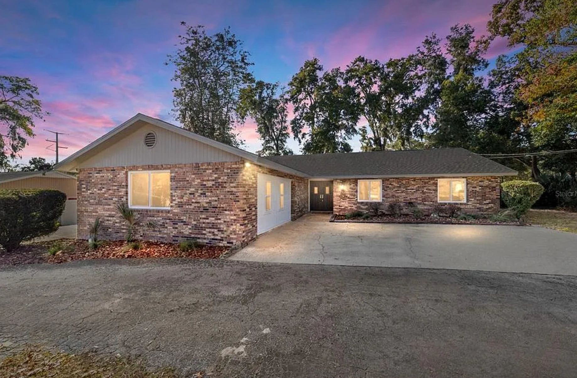 Single-story brick house at dusk with a driveway and illuminated windows.