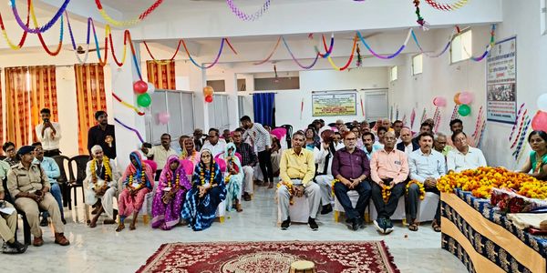Community gathering in a decorated hall with seated attendees and garlands.
