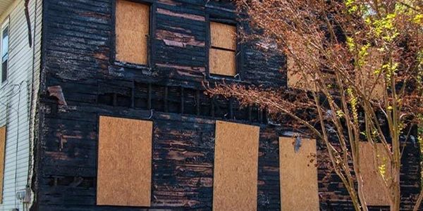 A fire-damaged house with boarded-up windows and walls.