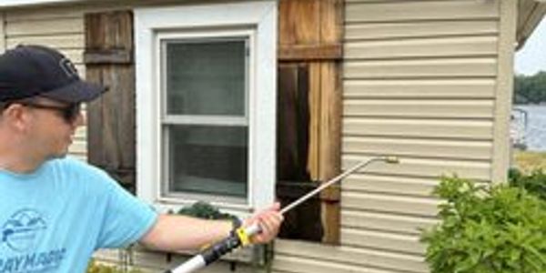 Man spraying pesticide on house exterior near plants.