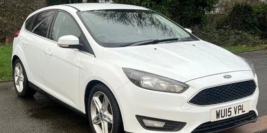 White Ford hatchback parked outdoors on a wet road.