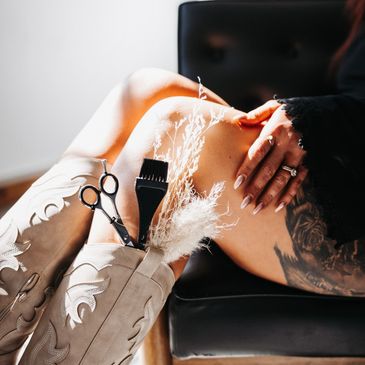 Person sitting with tattooed thigh and hairdressing tools in cowboy boots. hair stylist jobs