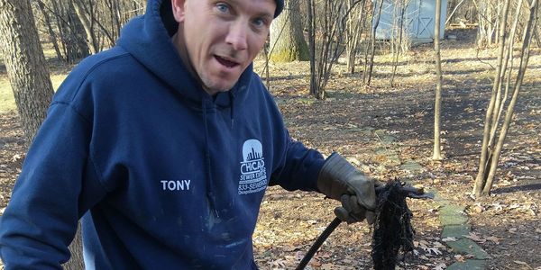 Man in blue hoodie holding a dirty garden tool outdoors.