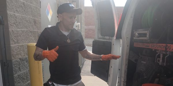 Man wearing orange gloves stands near an open van door.