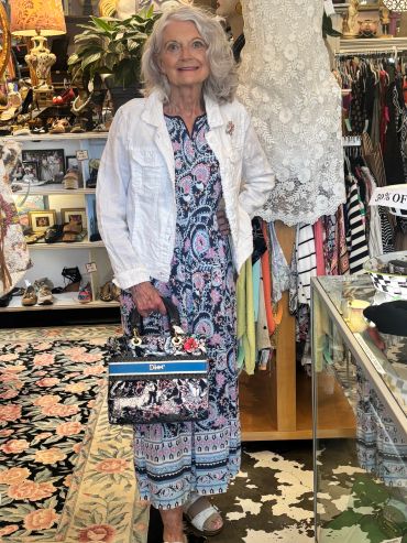 Elegant elderly woman posing in a boutique with a colorful dress and designer handbag.