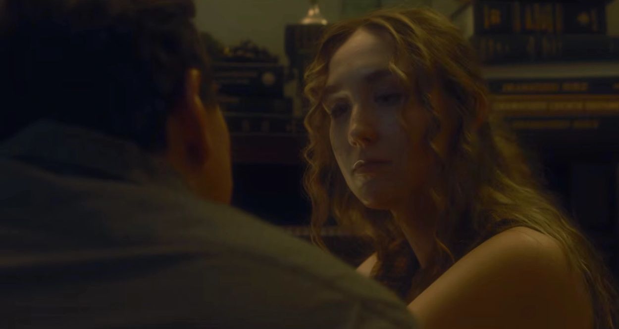 A woman with curly hair looks sadly at a man in a dimly lit room.