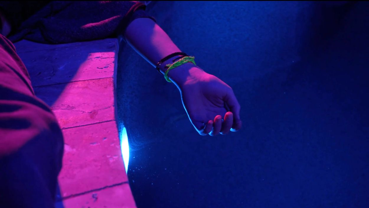 Hand over pool edge illuminated by blue light.