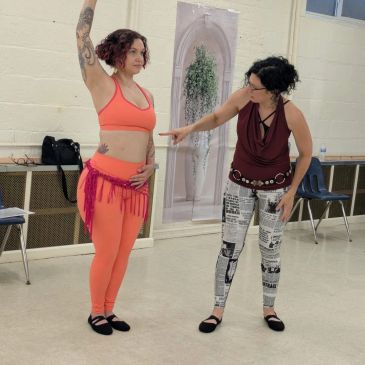 Two women practicing dance in a studio, one instructing the other.