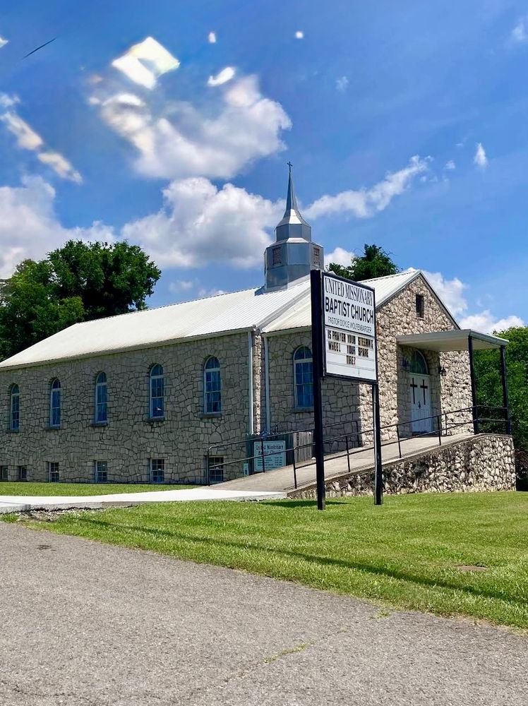 Stone church with a steeple and a welcoming sign under a blue sky.