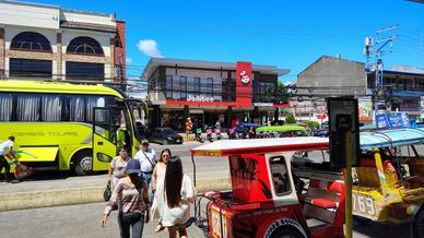 Street scene with people, a bright tour bus, and a Jollibee restaurant in the background.