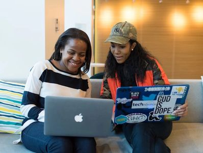 Two women happily working together on laptops in a cozy setting.