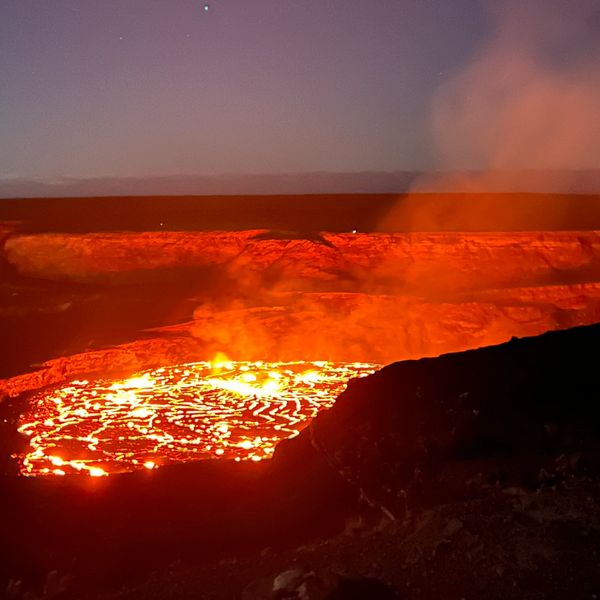 Night view of a glowing lava lake with smoke rising.