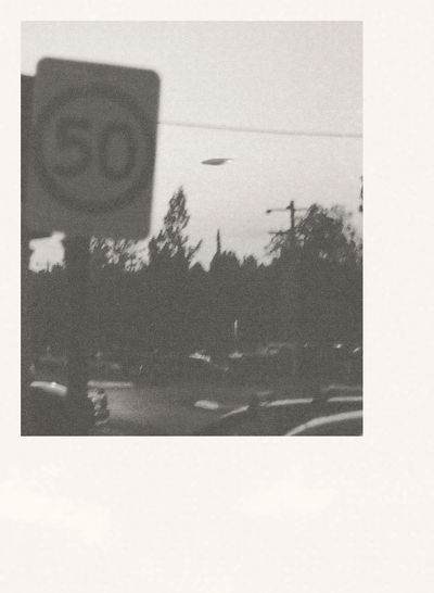 a grainy black and white photograph of a speed limit sign with a UFO in the background
