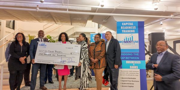 Group celebrating a check presentation at a business training event.