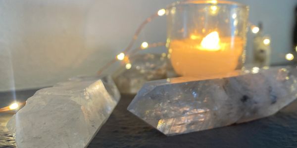 Two clear quartz crystals with a lit candle and string lights in the background.