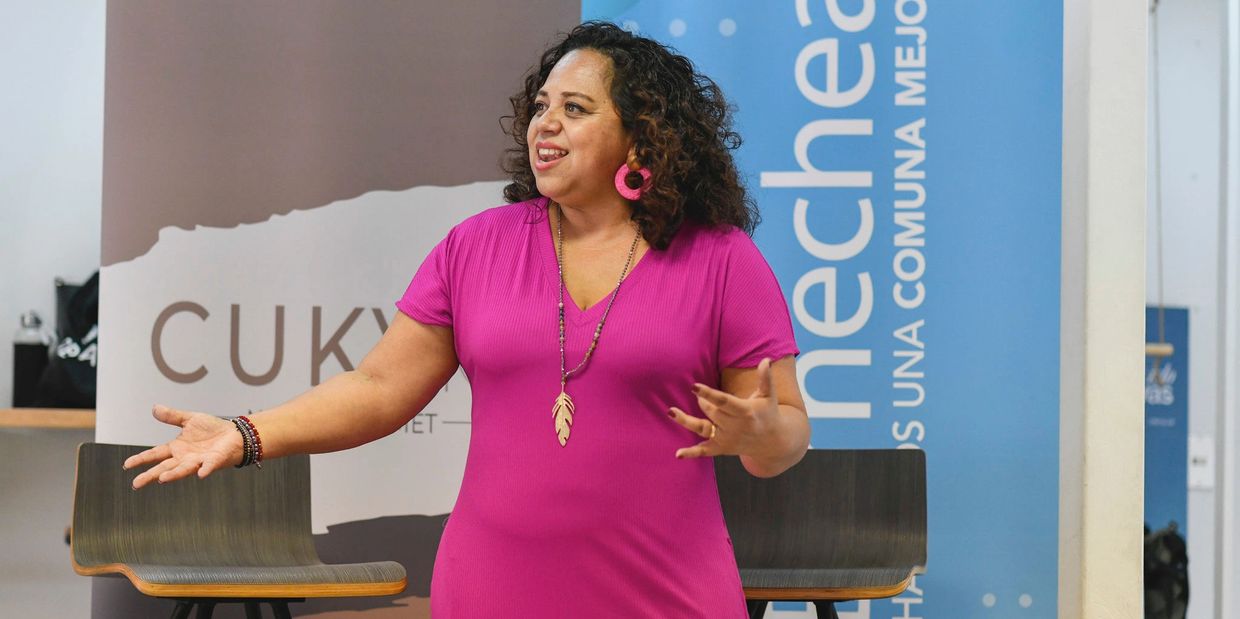 A woman in a pink dress speaking and gesturing during a presentation.
