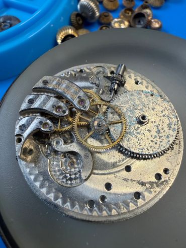 Close-up of an antique watch mechanism with rusted gears and components.