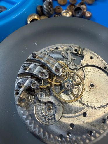 Close-up of a disassembled rusty watch mechanism with gears and screws.