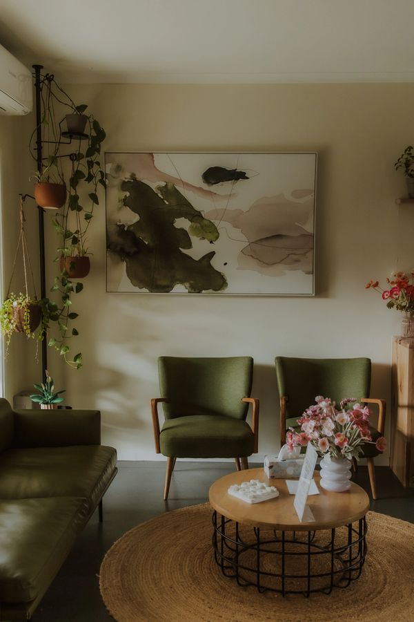 Cozy living room with green chairs, plants, and abstract wall art.
