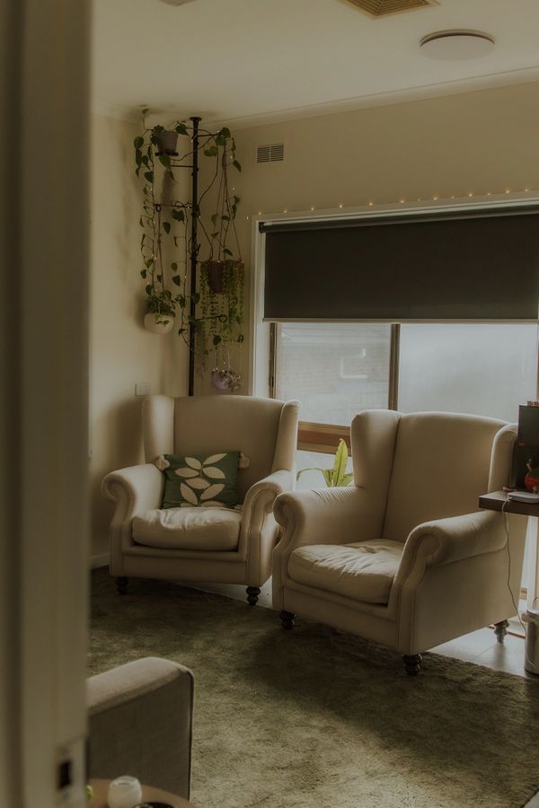Cozy living room with beige armchairs and hanging plants near a window.