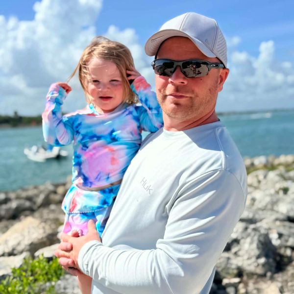 Man holding a young girl by the water on a sunny day.