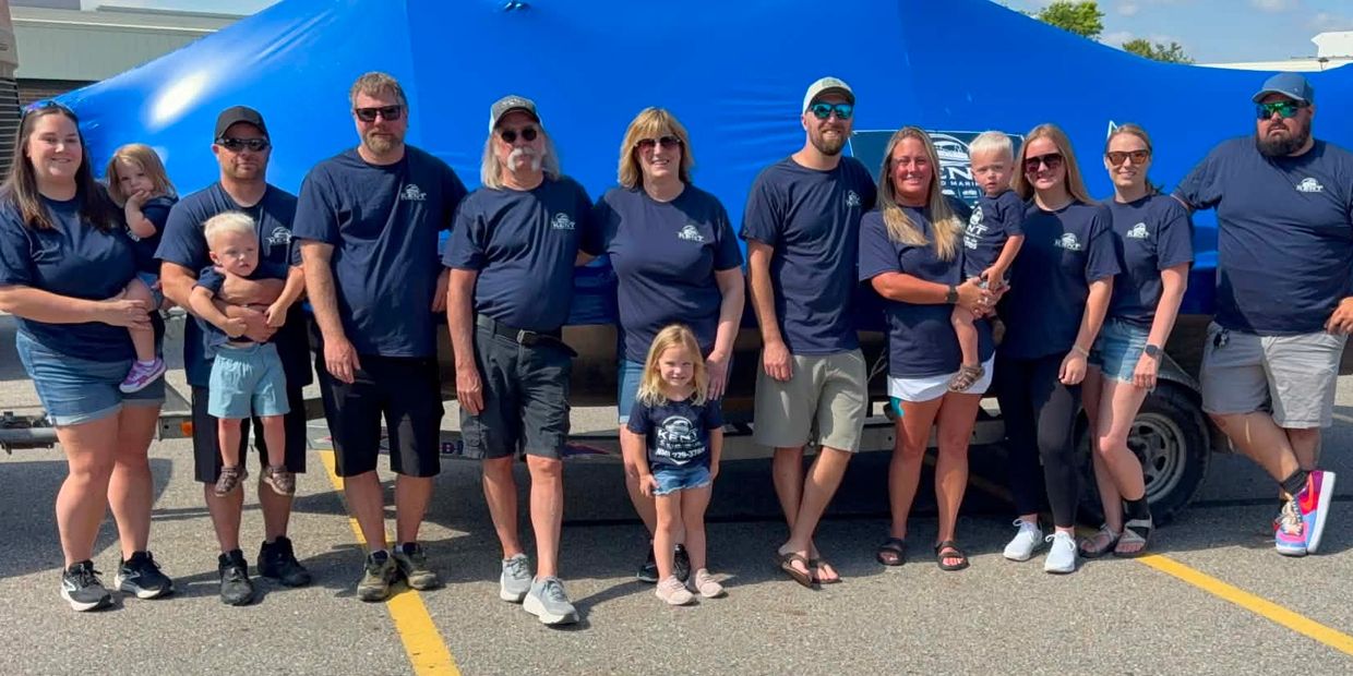 Group photo of people wearing matching blue shirts in front of a blue boat.