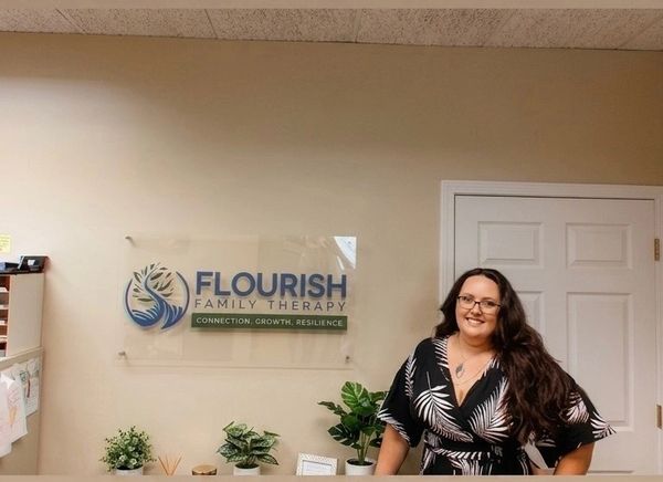 A woman smiling behind a reception desk at Flourish Family Therapy.