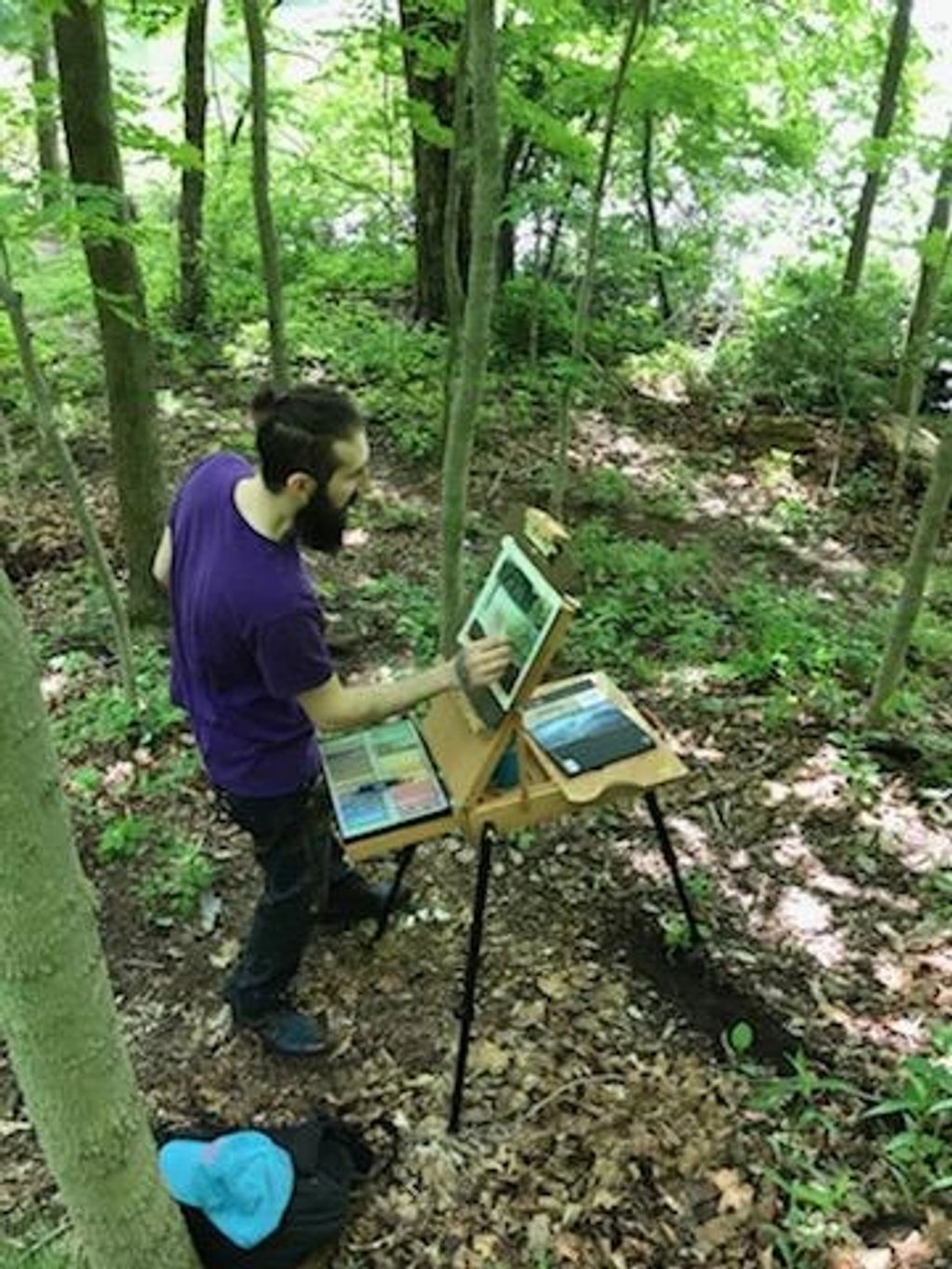 A man painting on an easel in a forest clearing.