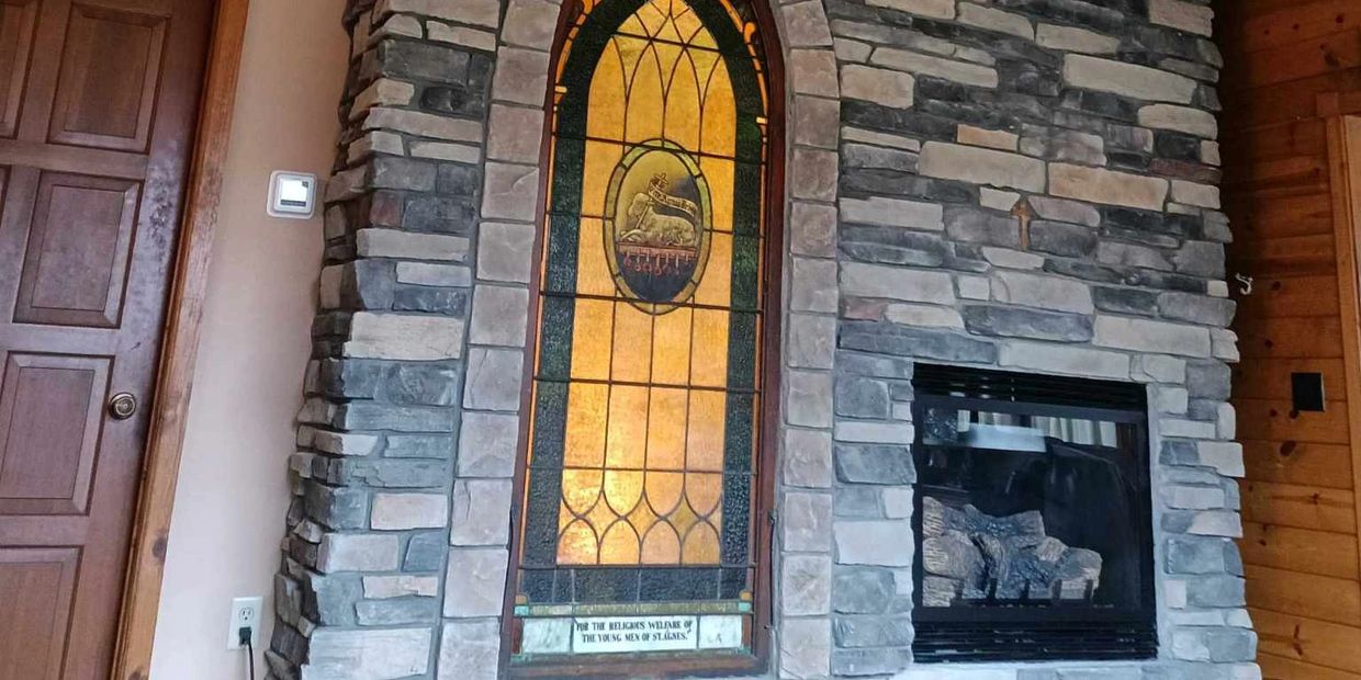 Stone fireplace with stained glass window feature in a wooden cabin interior.