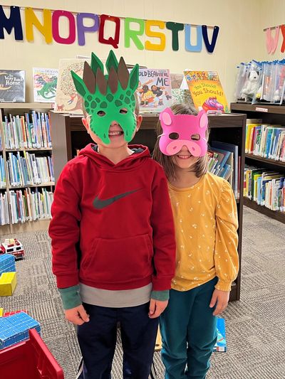 Two kids in the children's room wearing masks and smiling.