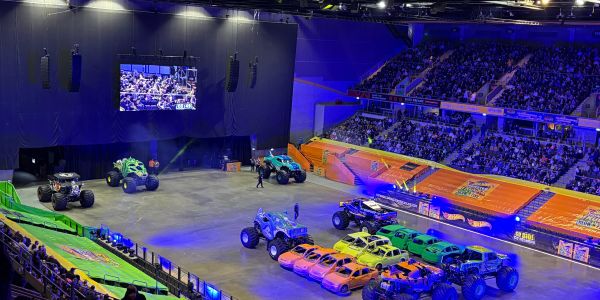 Monster trucks and crushed cars lined up in an arena with a large audience.
