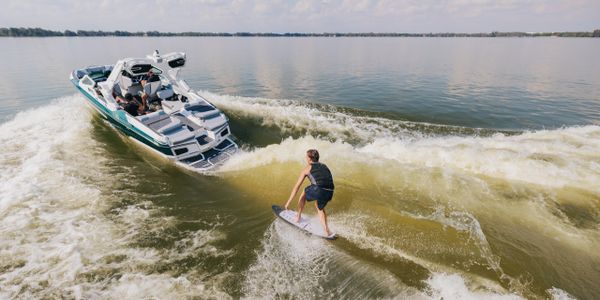 Person wakesurfs behind a boat on a calm lake.