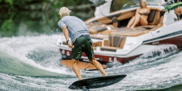 Man wakesurfing behind a boat on a lake with spectators.