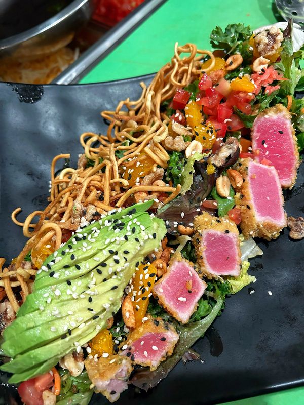 Fresh seared tuna salad with avocado, nuts, and crispy noodles on a black plate.