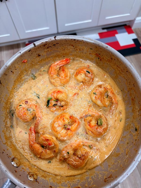 Shrimp cooking in a creamy, seasoned sauce in a saucepan.
