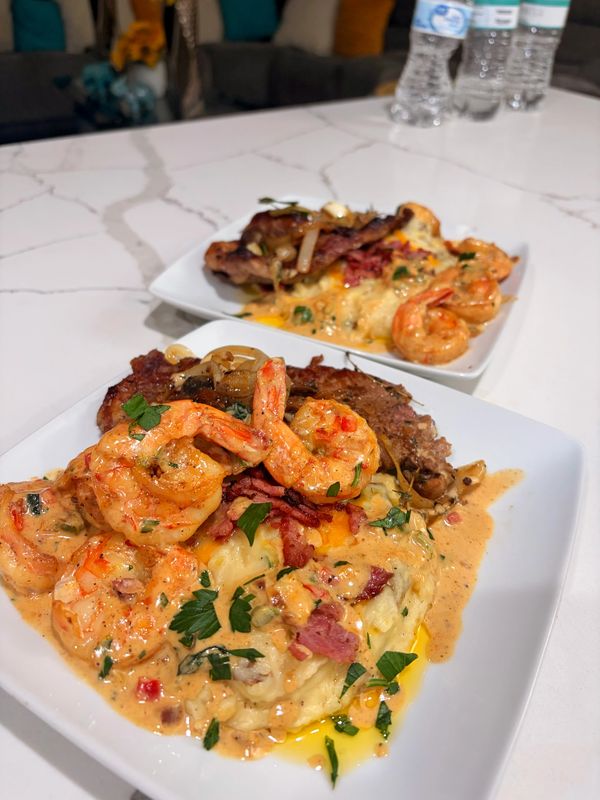 Plated shrimp and steak with creamy sauce and herbs on white dishes.