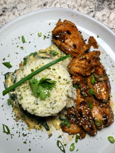 Plate with glazed chicken wings, seasoned rice, and garnished with herbs.