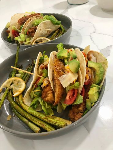 Plates of fish tacos with grilled asparagus and lemon slices.