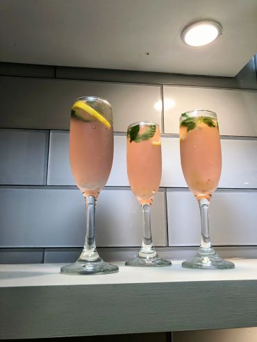 Three pink cocktails garnished with lemon and mint in champagne flutes.