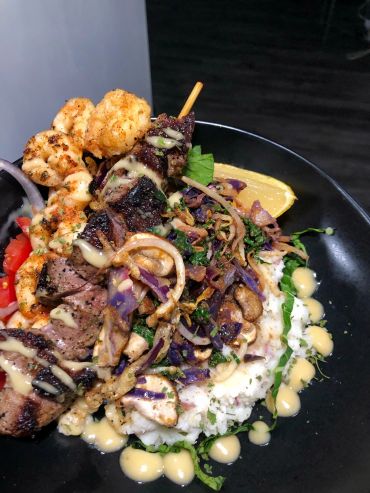 Grilled meat and cauliflower over rice with sauce and lemon wedge.