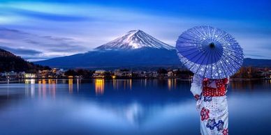 A woman in traditional Japanese dress looks at Mount Fuji across a lake.