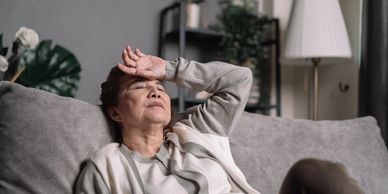 Lady on sofa, hands on forehead, visibly exhausted, showing symptoms of chronic fatigue syndrome.