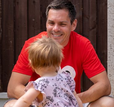 Picture of a man wearing a red t shirt and smiling at his daughter