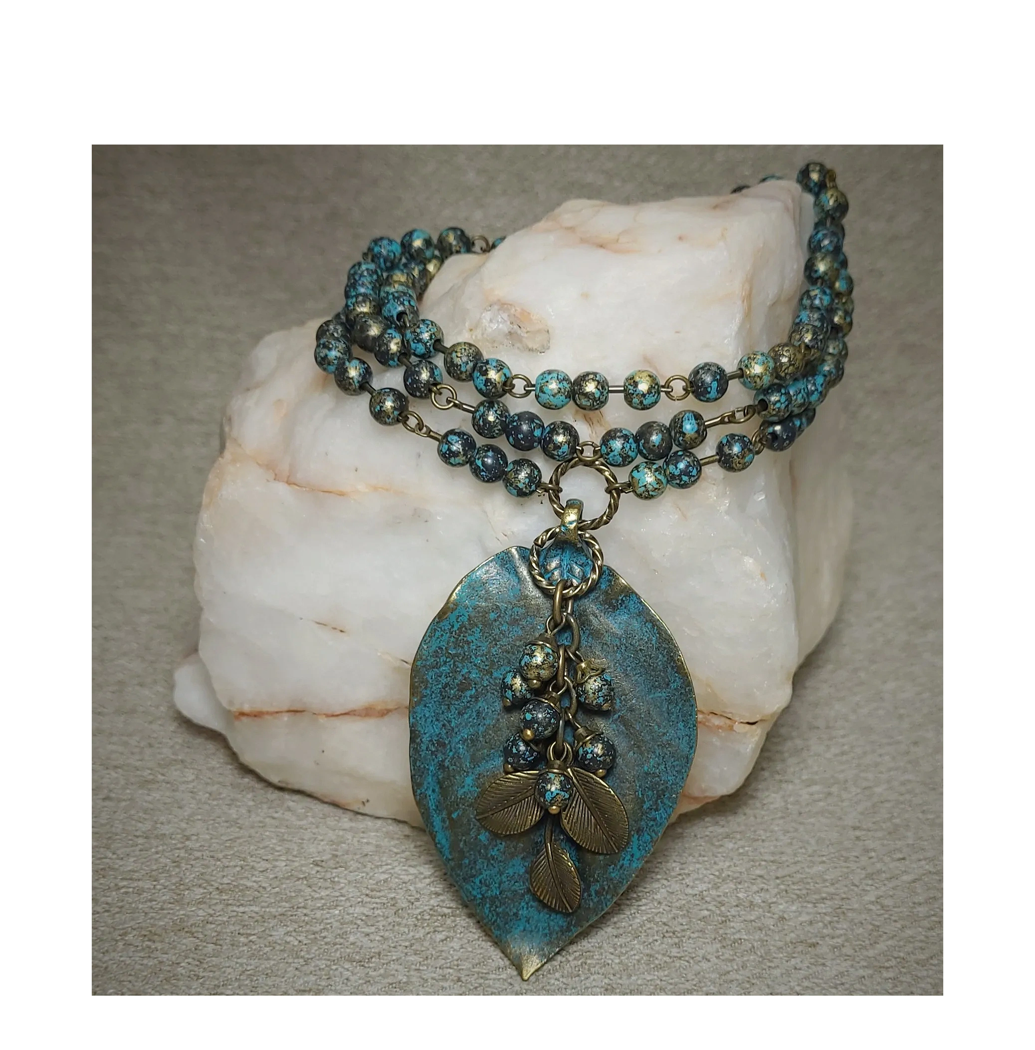 Long black and turquoise bead necklace with a large blue patina leaf pendant .