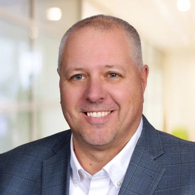 Smiling man in a blue checkered blazer and white shirt.