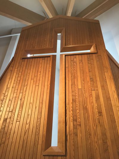A wooden wall with a cross-shaped cutout allowing light through.