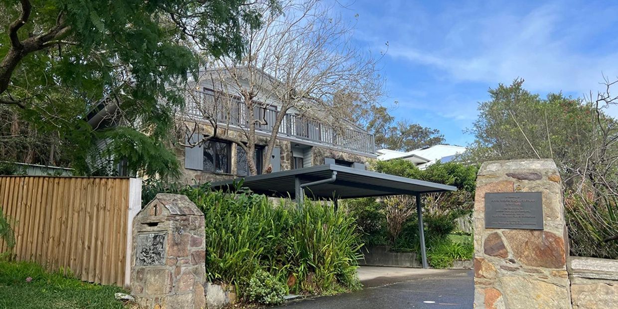Stone house with carport and greenery under a blue sky.