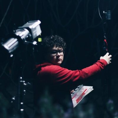 Person in a red hoodie adjusting studio lighting equipment in a dark setting.