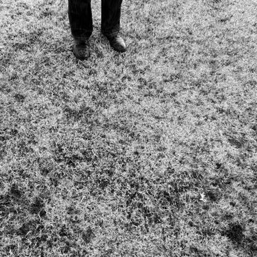 Black and white photo of feet on grass wearing shoes and pants.